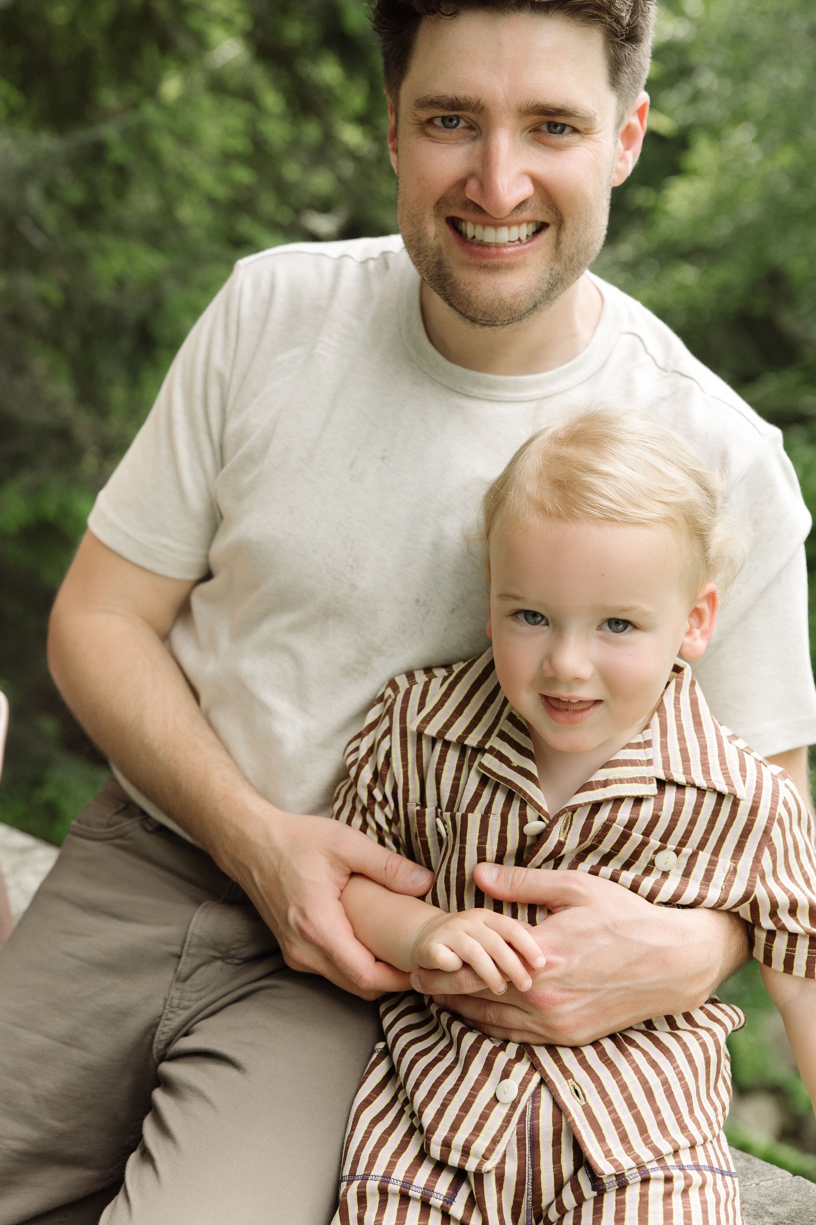 Dr. R.J. Stuart smiling outdoors while holding his young son Richie, who is wearing a brown striped shirt.