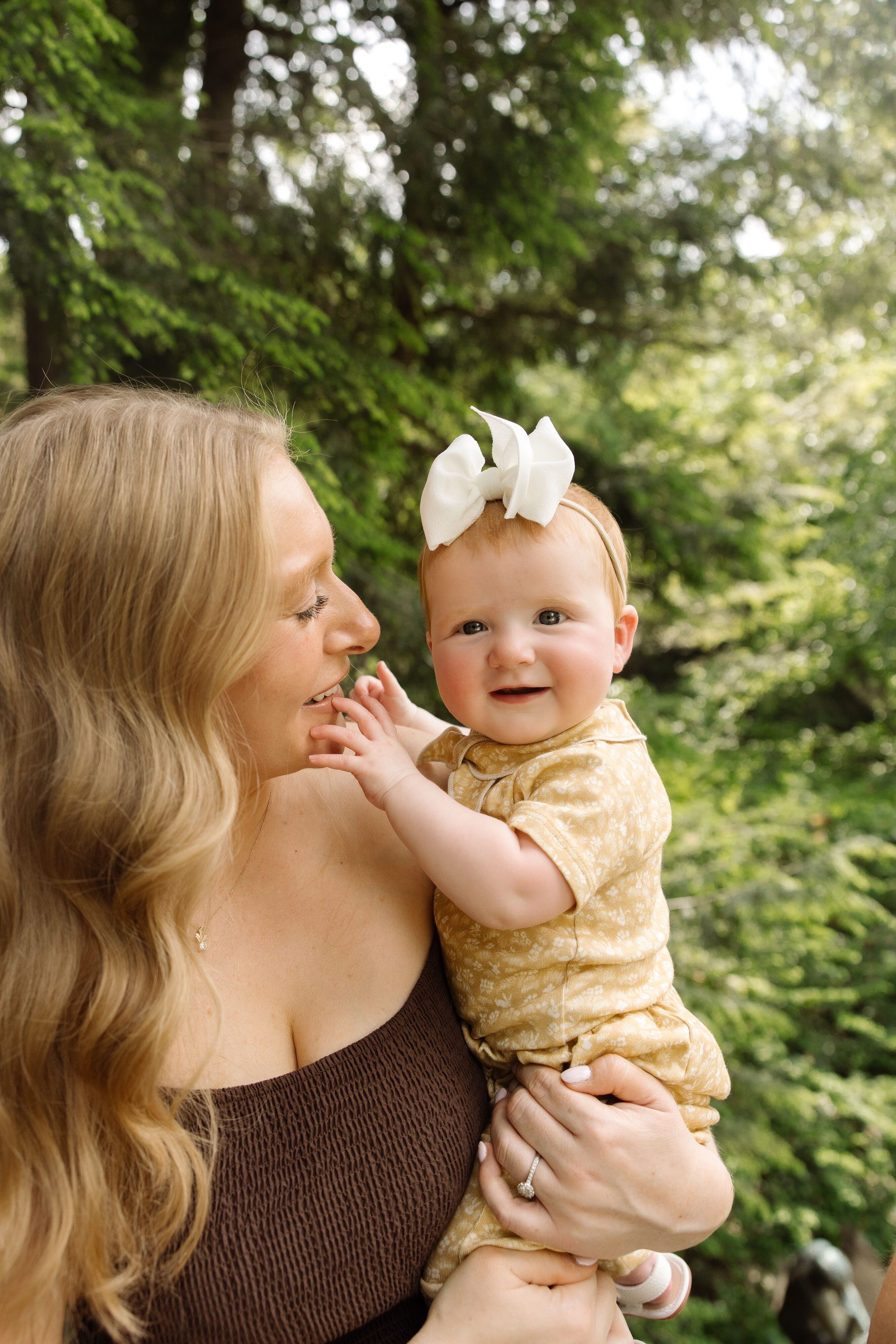 Mary Kate Stuart, Dr. Stuart's baby daughter, wearing a yellow outfit and a white bow, smiling while her mother Kathleen holds her outdoors.