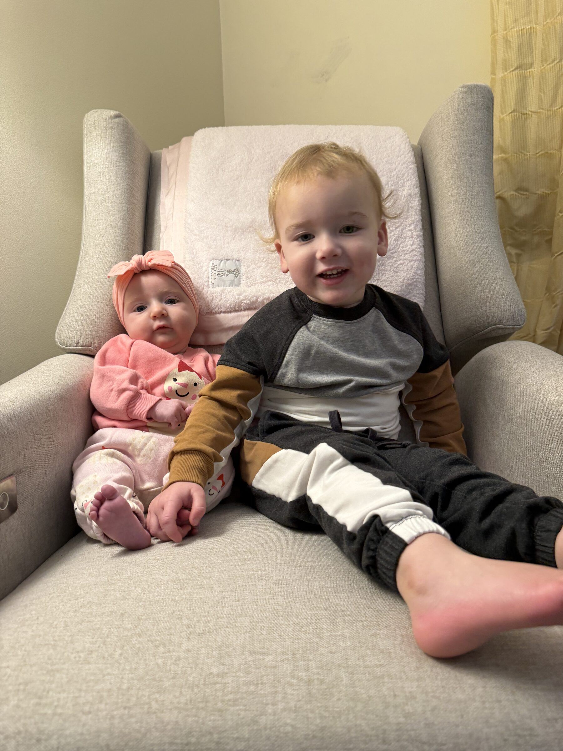 Richie Stuart, a smiling toddler, sitting next to his baby sister Mary Kate on a chair.